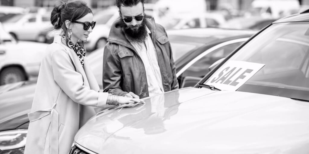 A young couple looking at a used car in a dealership lot.