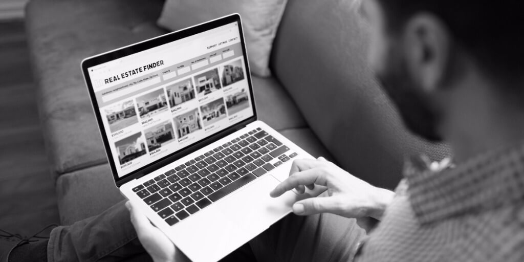 Person using a laptop to browse real estate listings online while seated on a couch.