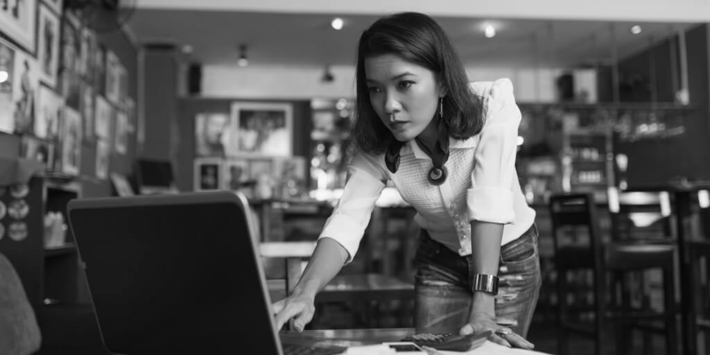 At Image Text	A concerned businesswoman is at a desk. She is holding a pen and looking at documents or paperwork in front of her. The background is a typical office setting with a computer and office supplies.