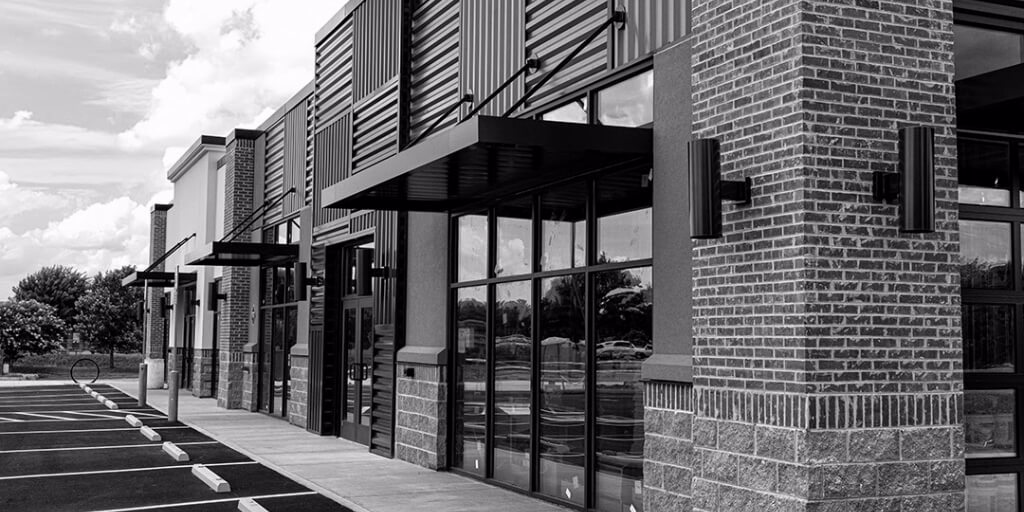 A corner view of the exterior of a brick building with three awnings and several windows is shown, as well as parking spaces